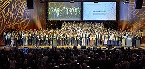 400 Absolventinnen und Absolventen jubeln bei ihrer Feier auf der Bühne, während Goldkonfetti auf sie regnet.